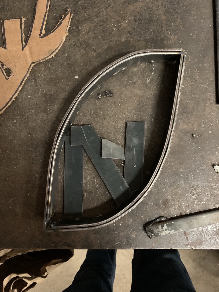 Steel strips laid out as an N inside a football-shaped border on a workshop table